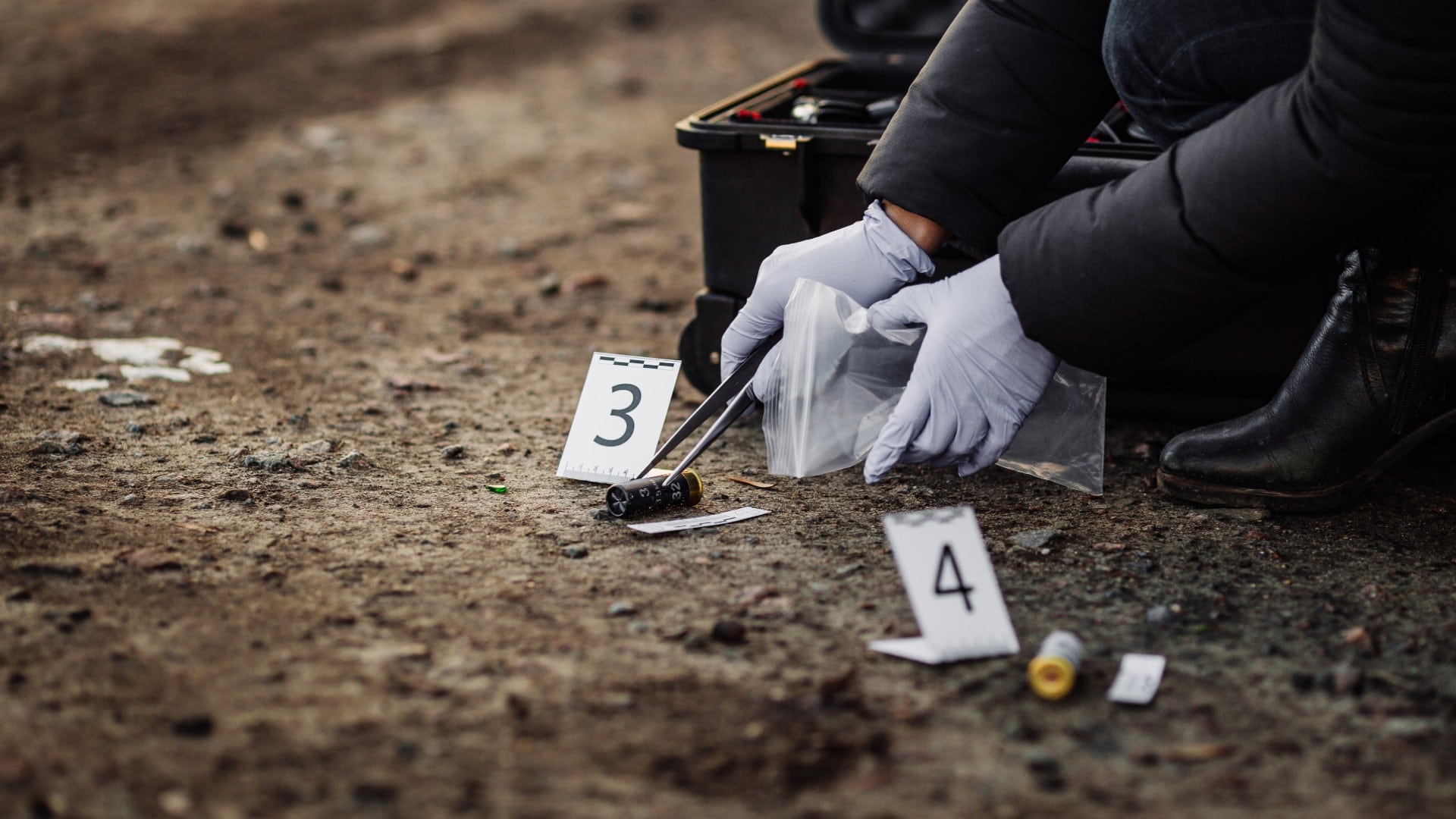Forensic investigator in gloves collecting evidence with numbered markers at an outdoor crime scene — the kind of investigation where GPR can map sub-surface anomalies