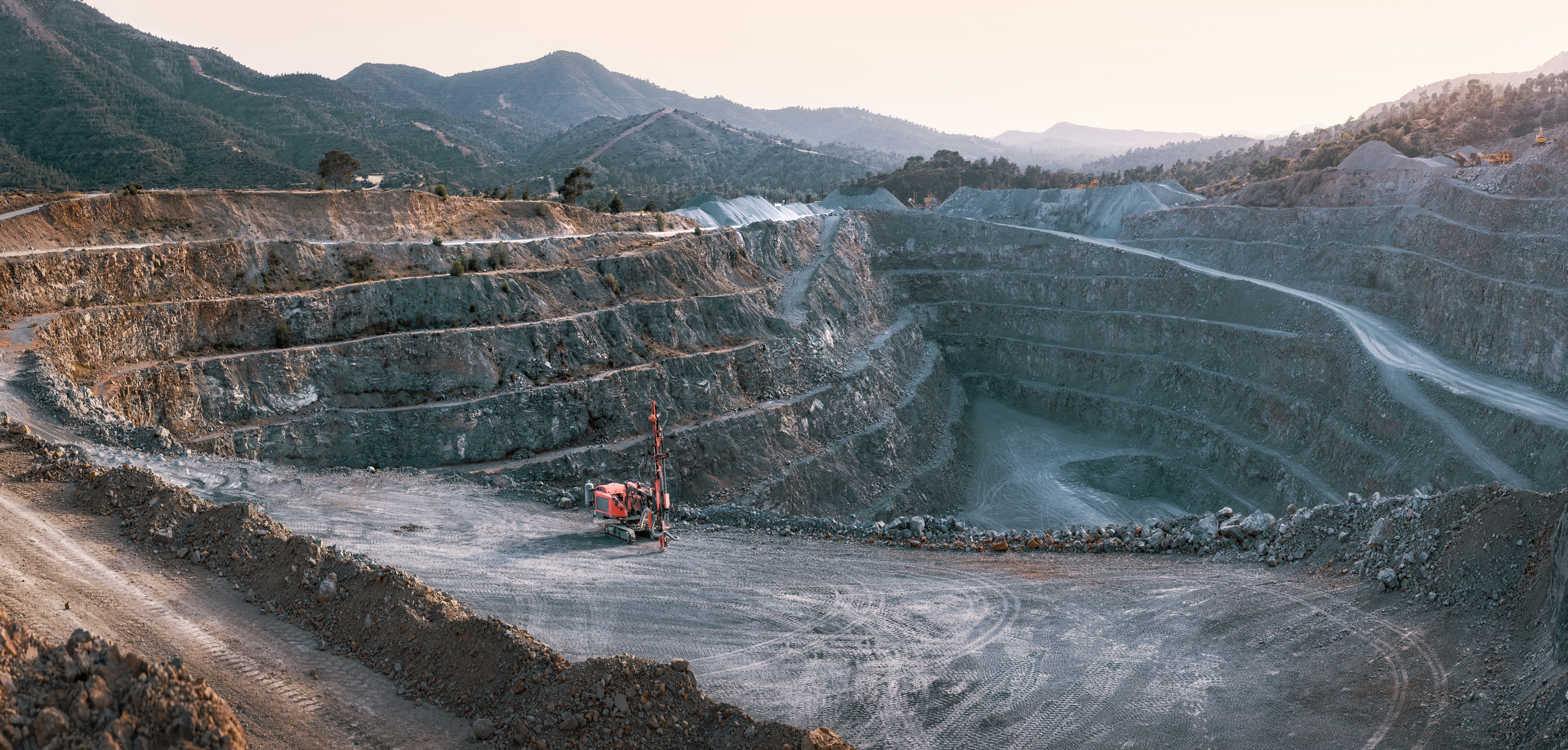 Open-pit gravel quarry with terraced benches and a red drill rig — exactly the kind of mining site where GPR maps ore bodies and subsurface geology layer by layer